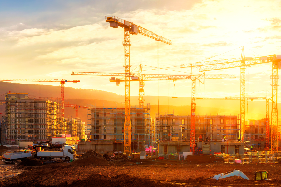 Large construction site including several cranes working on a building complex, illumined by warm gold sunlight Bild: de.stock.adobe.com/Smileus